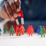 A hand holding a red horseshoe magnet to attract colorful human figures, symbolizing AGA's ability to pull in high-quality Medicare leads for agents.